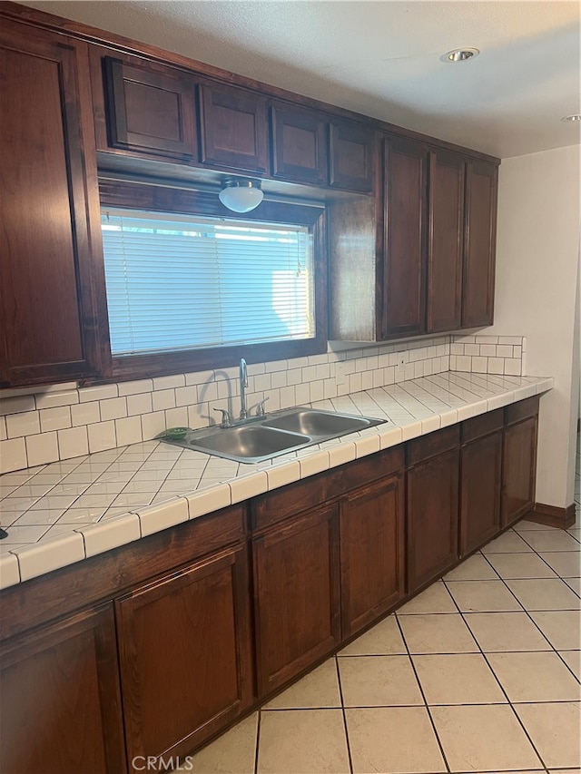 kitchen with decorative backsplash, dark brown cabinetry, light tile patterned floors, and sink