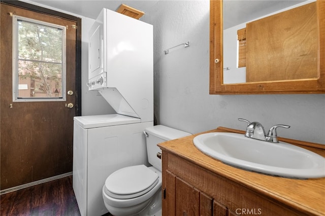 bathroom with toilet, vanity, stacked washer / drying machine, and hardwood / wood-style flooring