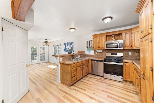 kitchen with sink, kitchen peninsula, light hardwood / wood-style flooring, backsplash, and appliances with stainless steel finishes