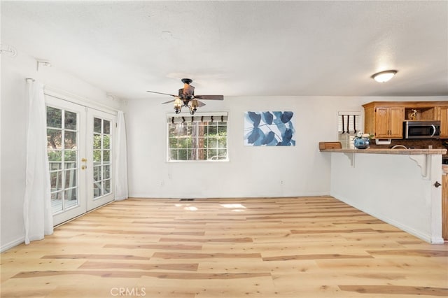 unfurnished living room featuring baseboards, light wood-style flooring, ceiling fan, a textured ceiling, and french doors