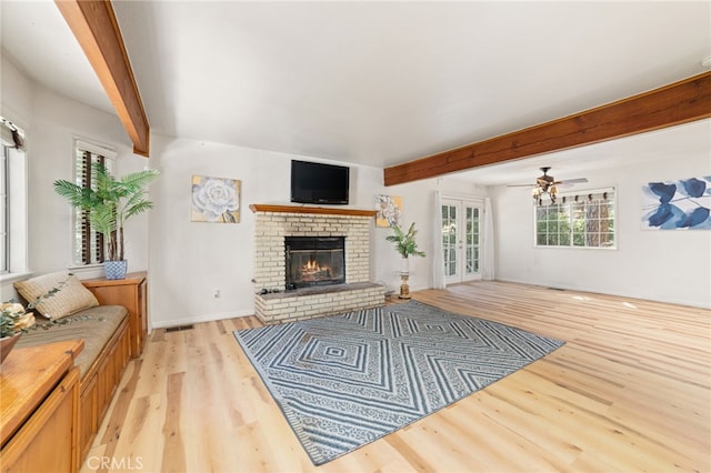 living room with ceiling fan, beamed ceiling, a fireplace, and light hardwood / wood-style floors