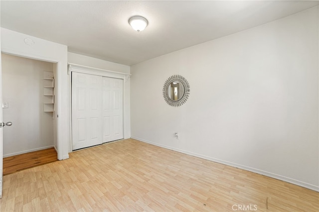 unfurnished bedroom featuring a closet, light wood-type flooring, and baseboards