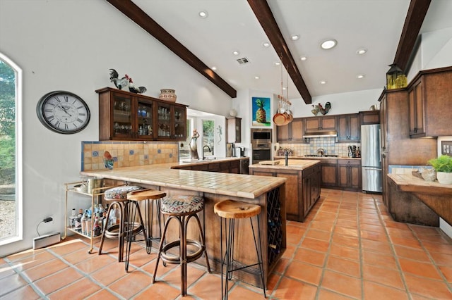 kitchen with vaulted ceiling with beams, backsplash, kitchen peninsula, a kitchen breakfast bar, and stainless steel appliances