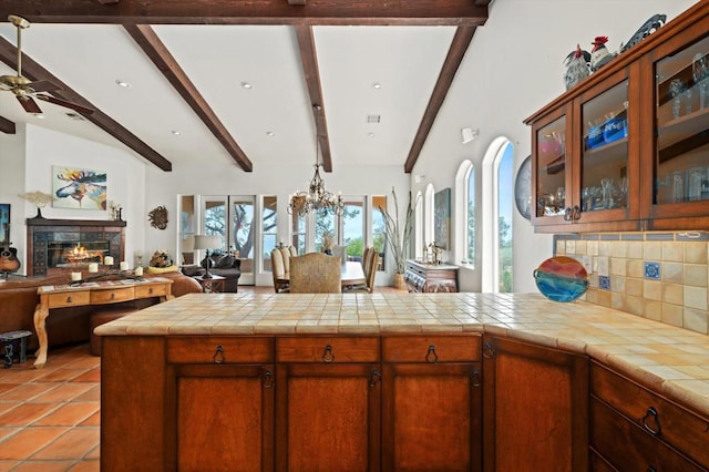 kitchen with kitchen peninsula, decorative backsplash, beam ceiling, tile countertops, and ceiling fan with notable chandelier