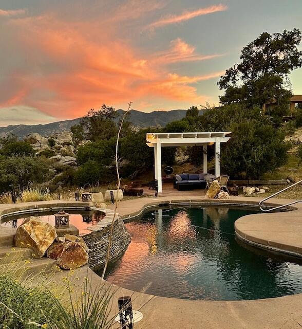 pool at dusk featuring a mountain view, a patio, and a pergola