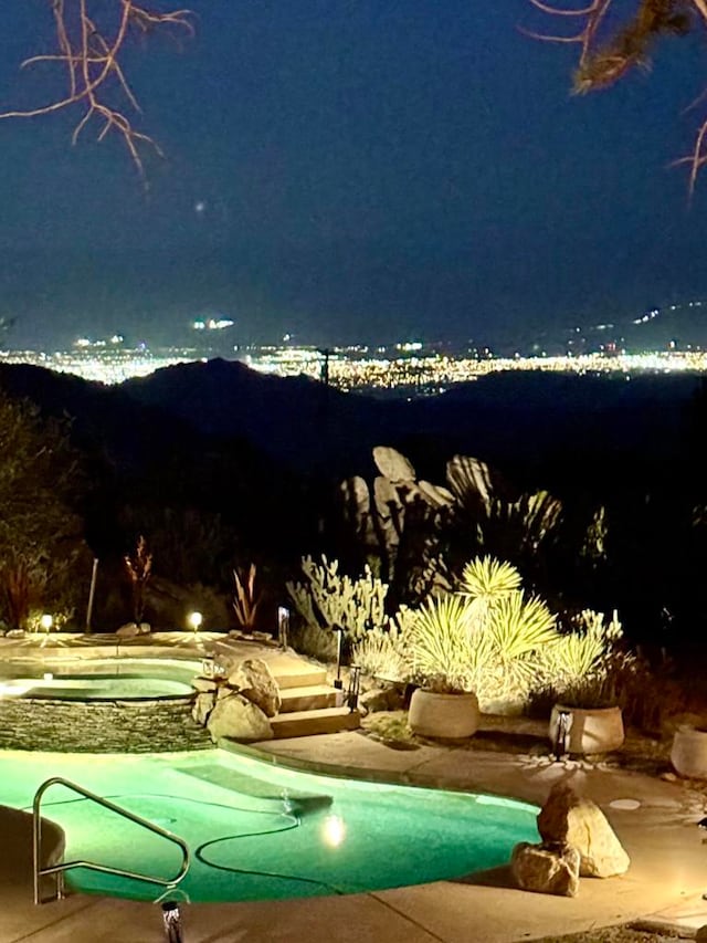 pool at night featuring an in ground hot tub