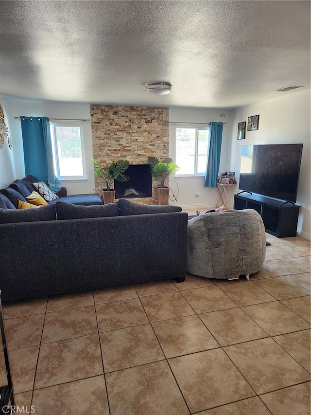 living room with a textured ceiling, a stone fireplace, and tile patterned floors