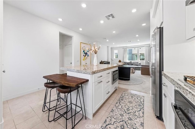 kitchen with light stone counters, stainless steel appliances, light tile patterned floors, white cabinets, and a center island