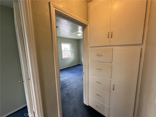 hall featuring dark colored carpet and a textured ceiling