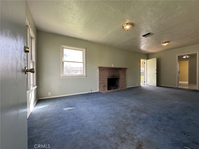 unfurnished living room with dark colored carpet, a textured ceiling, and a brick fireplace