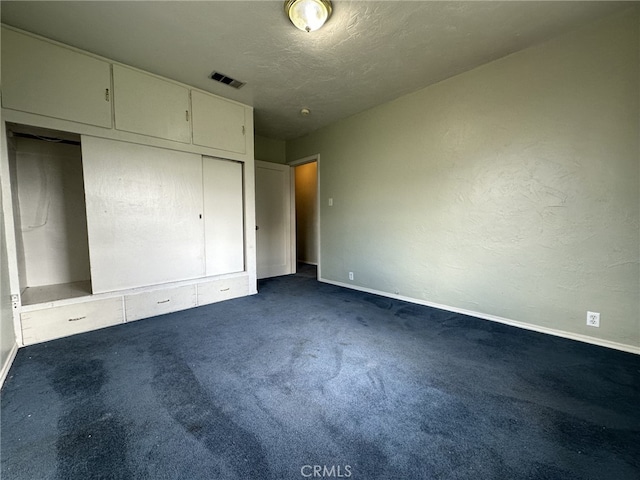 unfurnished bedroom featuring a closet, dark carpet, and a textured ceiling