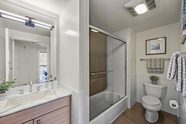 full bathroom featuring tile walls, vanity, shower / bath combination with glass door, and toilet