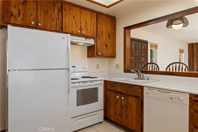 kitchen featuring under cabinet range hood, white appliances, a sink, light countertops, and brown cabinetry