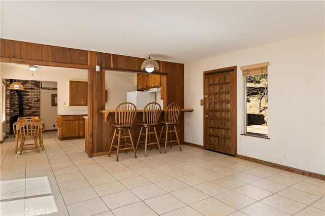 kitchen with light tile patterned floors, a kitchen bar, white fridge, and a wood stove