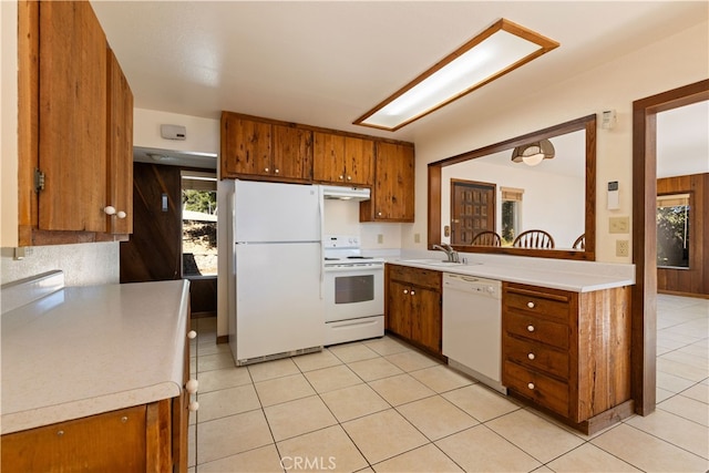 kitchen featuring light countertops, brown cabinetry, a sink, white appliances, and under cabinet range hood