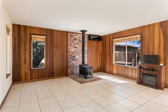 unfurnished living room featuring light tile patterned flooring, wood walls, and a wood stove