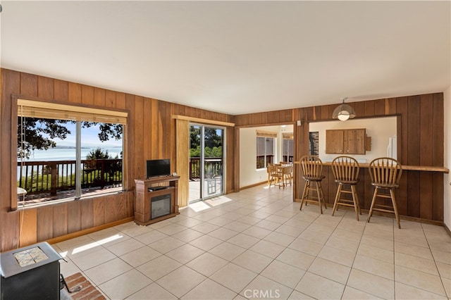 living area featuring wooden walls, baseboards, a glass covered fireplace, and light tile patterned flooring