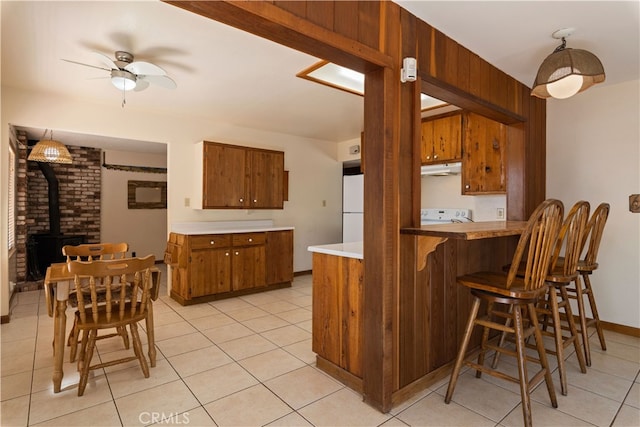 kitchen with light tile patterned flooring, kitchen peninsula, pendant lighting, a wood stove, and stove