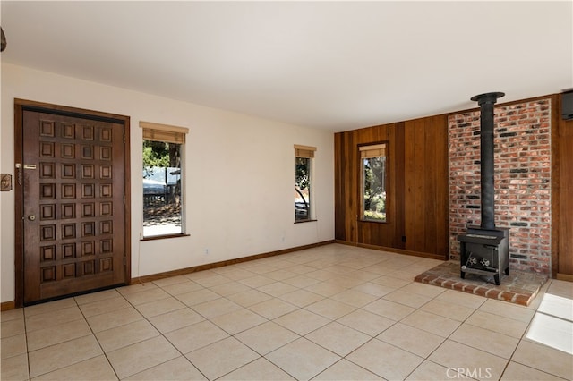 entrance foyer featuring a wood stove, light tile patterned floors, baseboards, and wood walls