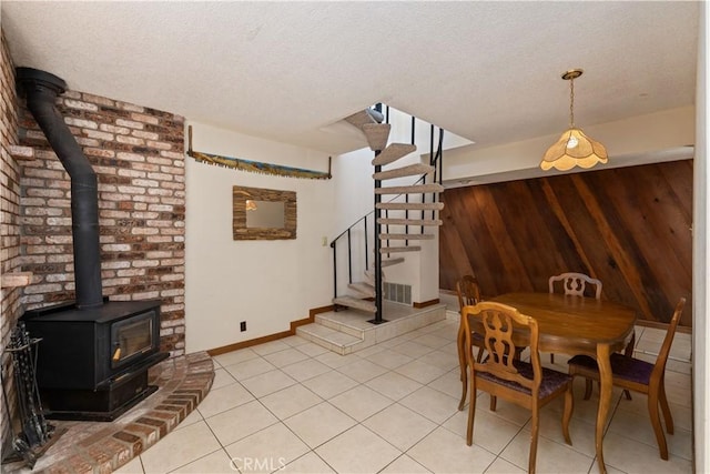 dining area with light tile patterned floors, a wood stove, a textured ceiling, baseboards, and stairs