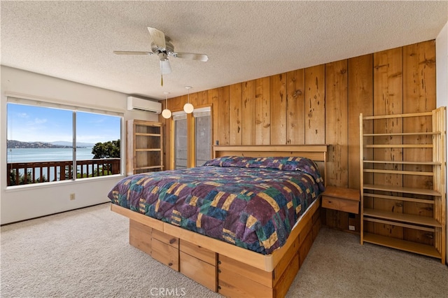 bedroom with a water view, an AC wall unit, ceiling fan, carpet, and wooden walls