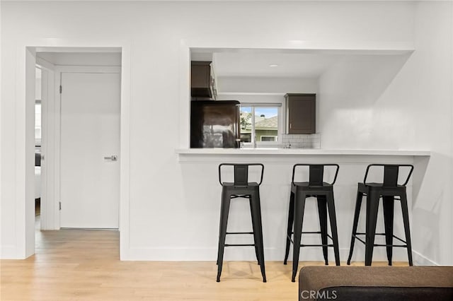 kitchen with tasteful backsplash, kitchen peninsula, light hardwood / wood-style floors, fridge, and a breakfast bar