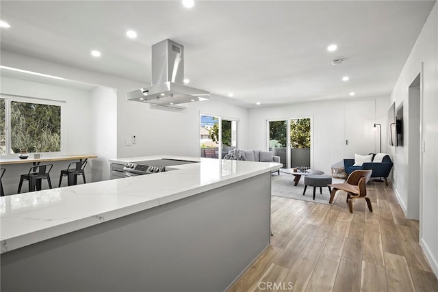 kitchen with light stone countertops, kitchen peninsula, extractor fan, stainless steel electric range, and light wood-type flooring