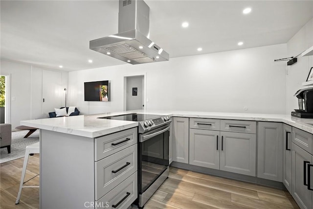 kitchen with stainless steel electric stove, light hardwood / wood-style floors, light stone counters, kitchen peninsula, and island exhaust hood