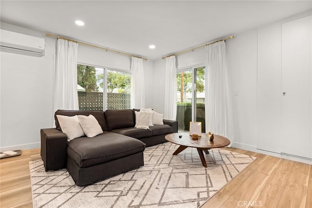 living room featuring light hardwood / wood-style flooring, a wall unit AC, and a healthy amount of sunlight