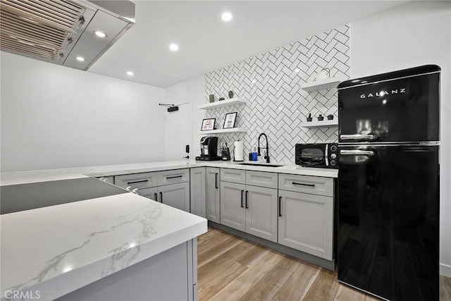 kitchen featuring gray cabinetry, sink, black fridge, light hardwood / wood-style flooring, and extractor fan