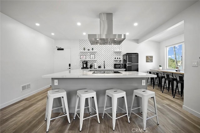 kitchen with hardwood / wood-style floors, wall chimney exhaust hood, a kitchen breakfast bar, and tasteful backsplash