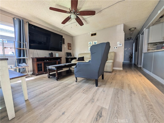 living room with visible vents, a ceiling fan, light wood-style floors, baseboards, and a textured ceiling