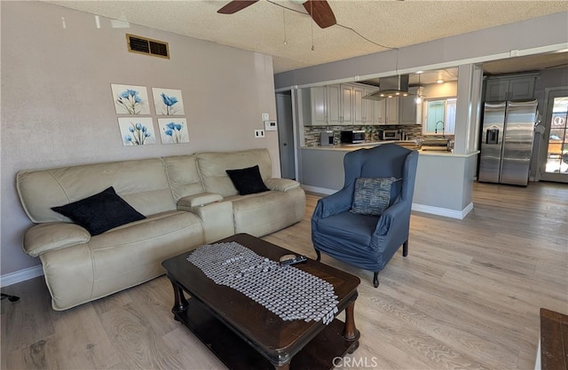 living area with a textured ceiling, light wood-style flooring, visible vents, and a ceiling fan
