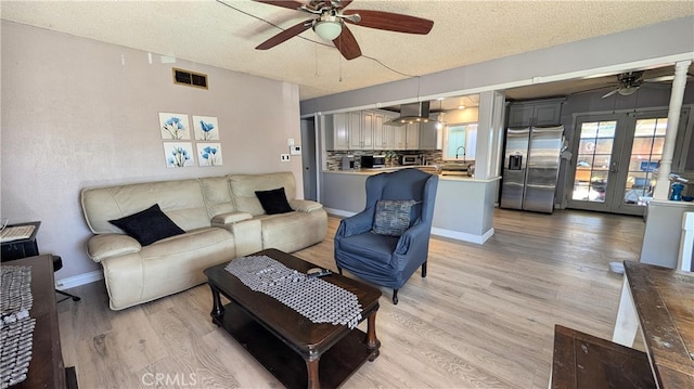 living room with a ceiling fan, visible vents, a textured ceiling, and light wood-style flooring
