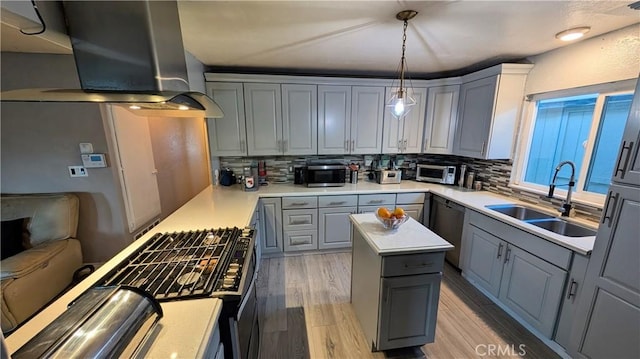 kitchen with a sink, decorative backsplash, gray cabinetry, wall chimney range hood, and appliances with stainless steel finishes