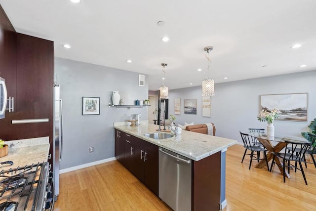 kitchen with stainless steel appliances, light stone countertops, pendant lighting, light hardwood / wood-style flooring, and sink