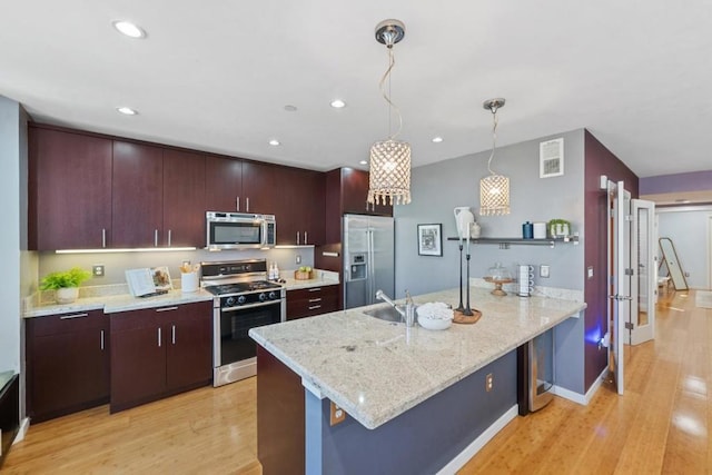 kitchen featuring light hardwood / wood-style flooring, kitchen peninsula, appliances with stainless steel finishes, hanging light fixtures, and light stone counters