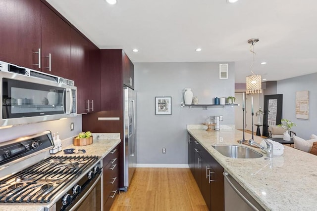 kitchen featuring appliances with stainless steel finishes, light stone countertops, pendant lighting, light hardwood / wood-style flooring, and sink