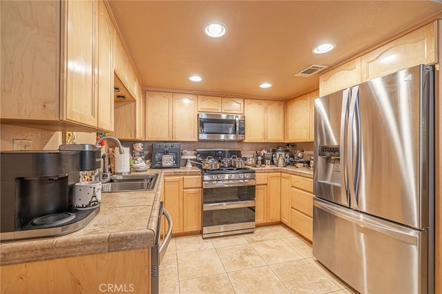 kitchen with light tile patterned flooring, appliances with stainless steel finishes, light brown cabinetry, and sink