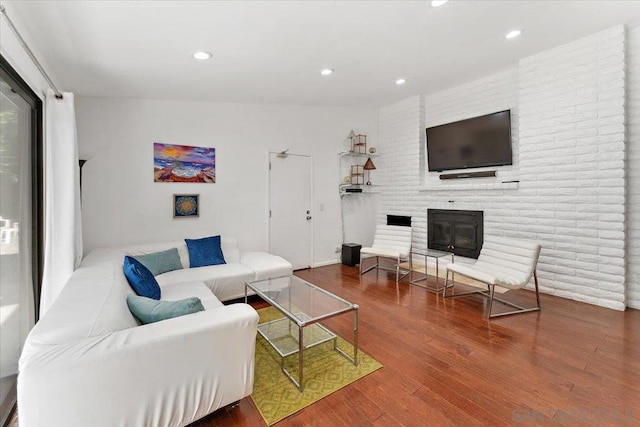 living room with a brick fireplace, vaulted ceiling, and hardwood / wood-style floors