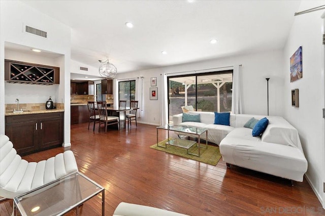 living room with wet bar, a chandelier, and dark wood-type flooring