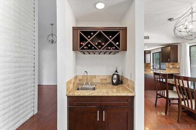 bar with light stone counters, dark hardwood / wood-style floors, sink, an inviting chandelier, and decorative light fixtures