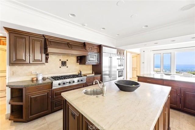 kitchen with built in appliances, a center island with sink, custom range hood, and sink