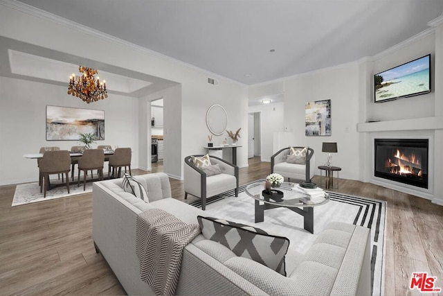 living room with wood-type flooring, crown molding, and an inviting chandelier