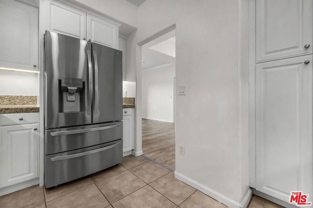 kitchen featuring stainless steel fridge, light tile patterned floors, and white cabinets