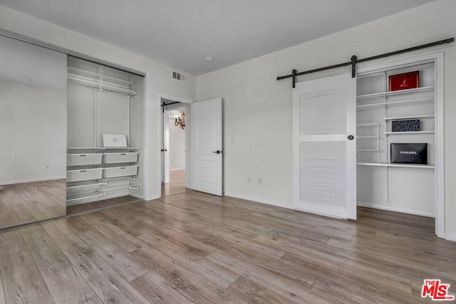 unfurnished bedroom featuring a barn door, a closet, and light hardwood / wood-style floors