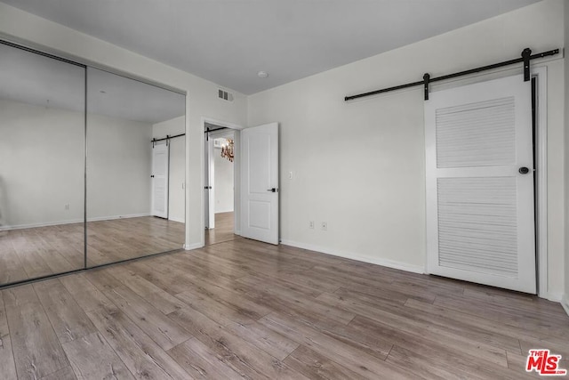 unfurnished bedroom featuring light hardwood / wood-style floors, a closet, and a barn door