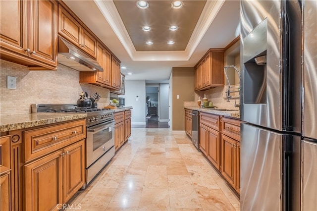 kitchen with appliances with stainless steel finishes, light stone counters, backsplash, and a raised ceiling