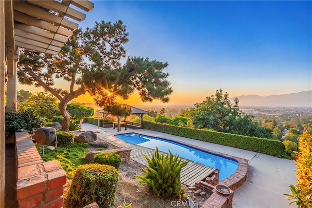 pool at dusk featuring a gazebo, a patio area, and a mountain view