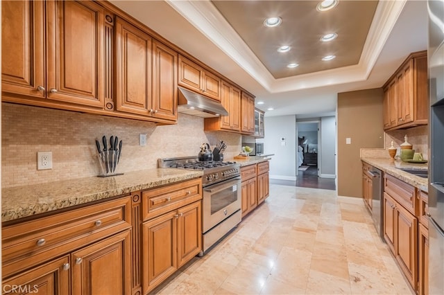 kitchen featuring light stone counters, a raised ceiling, backsplash, appliances with stainless steel finishes, and crown molding